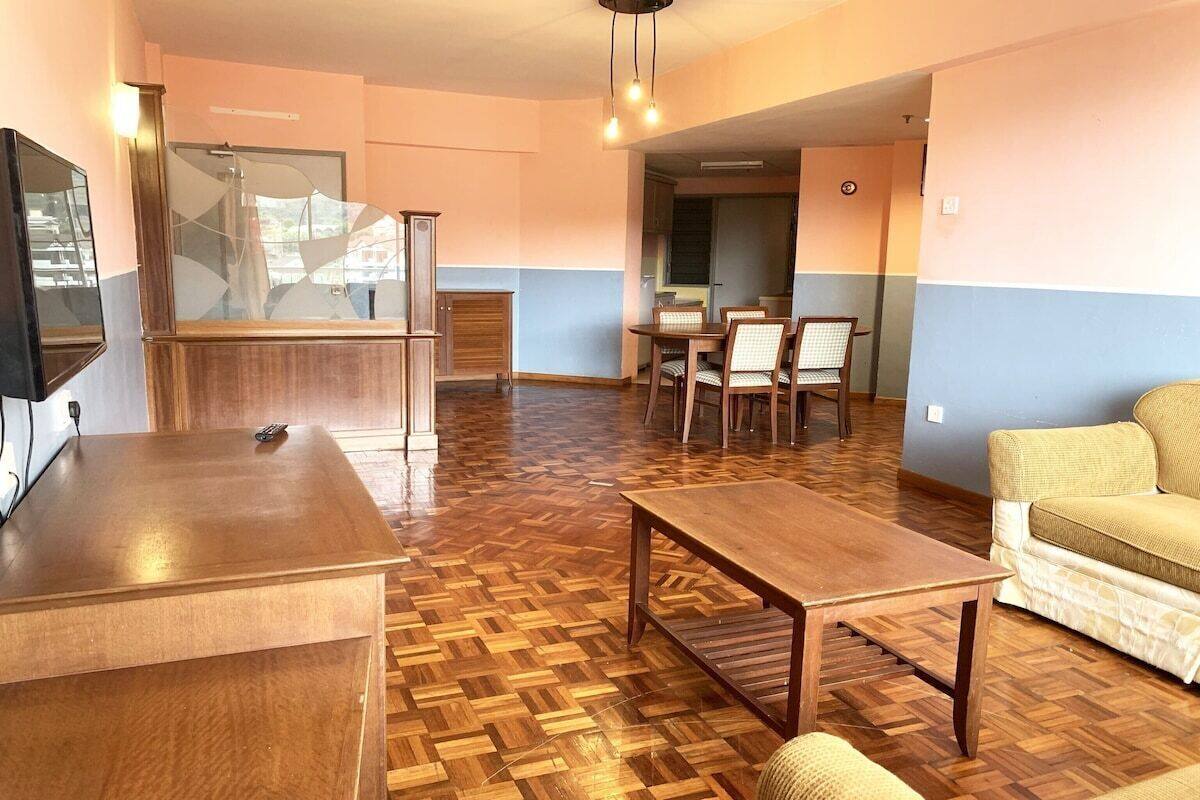 A spacious living area with a wooden floor, a sofa, a coffee table, and a dining table with chairs.