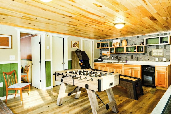 A cozy room with wooden flooring, a foosball table, and a kitchen area with wooden cabinets and a built-in oven.