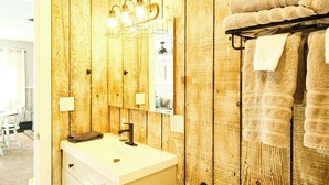 A bathroom with wooden panel walls, a white sink, a mirror, and a towel rack with towels. - Winter Vacation Chalet at Powderhorn Mountain (Ironwood Township)
