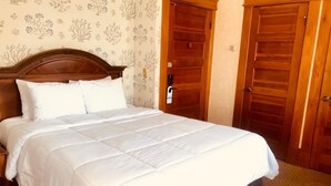 A neatly made bed with white bedding in a room with floral wallpaper and wooden doors.