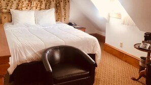 A bedroom with a large bed, a black leather chair, a patterned carpet, and a small table with a lamp.