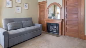 A room with a grey sofa, a fireplace, wooden doors, and framed artwork on the wall. - Blocks from Ocean - KING BEDROOM SUITE (PACIFIC GROVE)