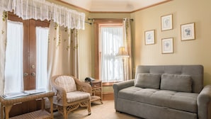 A room with a grey sofa, wicker chairs, a glass-top table, and a window with curtains. - Blocks from Ocean - KING BEDROOM SUITE (PACIFIC GROVE)