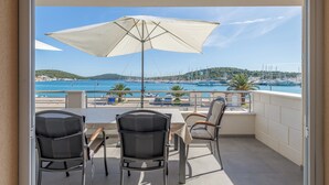 Een balkon met een tafel en stoelen, een grote parasol en uitzicht op zee en boten.