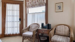 Ein Zimmer mit zwei Korbstühlen, einem kleinen Tisch mit Kaffeemaschine, einem Mülleimer und einer Tür mit satiniertem Glasfenster.