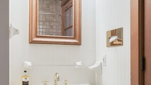 Ein Badezimmer mit einem weißen Waschbecken, einem spiegel mit Holzrahmen und zwei Wandleuchten.