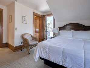 A hotel room with a large bed, a wicker chair, a small table with a lamp, and a door leading outside. - CROSS Ocean View from Balcony-RELAX-QUEEN BEDROOM (PACIFIC GROVE)