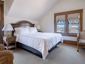 Un dormitorio con una cama, dos mesitas de noche, un ventanal con vistas y muebles de mimbre.