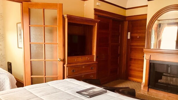 A hotel room with a large bed, a wooden wardrobe, a fireplace, and a door with frosted glass panels.