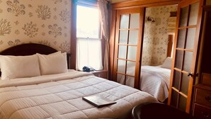 A hotel room with a large bed, a desk, and a chair. There is a window with curtains, a door with glass panels, and floral wallpaper.