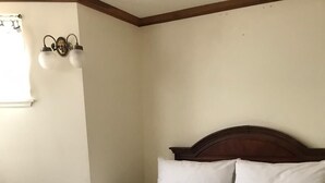 Una cama bien hecha con edredón blanco y dos almohadas, un cabecero de madera y una mesita de noche con un libro.