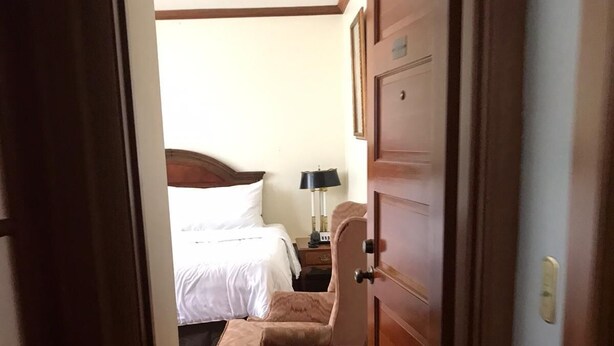 Una habitación de hotel con una cama, una mesita de noche, una lámpara y una silla.