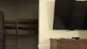 A bedroom with a bunk bed, a dresser, and a TV mounted on the wall. - Queen Bed with Bunk bed (PACIFIC GROVE)