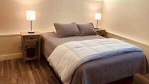 A bedroom with a bed, two bedside tables, a nightstand, a window, and a wooden floor. - Queen Bed with Bunk bed (PACIFIC GROVE)