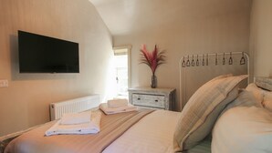 Een slaapkamer met een bed, een nachtkastje, een aan de muur bevestigde televisie en een radiator.