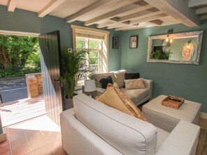 A living room with a sofa, a coffee table, and a potted plant. There is a window with blinds and a door leading outside. - Number 4 (Telford)