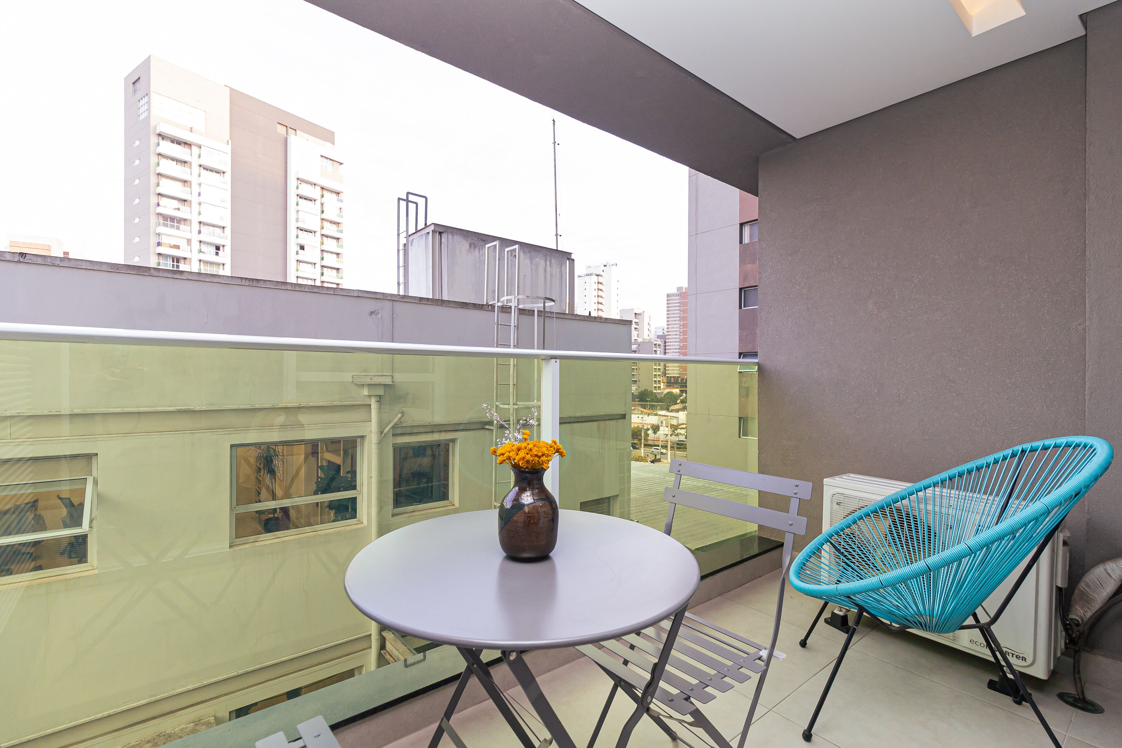 A balcony with a round table, a vase with flowers, a blue chair, and a radiator.