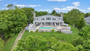 Une grande maison à deux étages, dotée d’une piscine, entourée d’une végétation luxuriante et d’arbres.