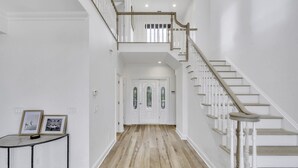 Un couloir avec un escalier en bois, des murs blancs et une porte dotée de panneaux de verre.