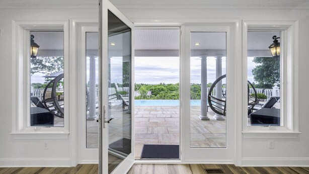 Une pièce dotée d’une porte-fenêtre coulissante donnant sur un patio extérieur avec une piscine, des colonnes et du mobilier d’extérieur.