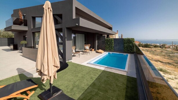 Een modern huis met een zwembad, terras en uitzicht op zee.