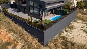 Ett modernt hus i två våningar med en pool på taket, stora fönster och ett platt tak.
