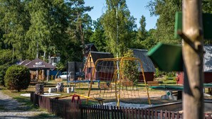 Un parque infantil con columpios y una estructura para escalar, rodeado de árboles y una valla de madera.