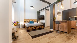 Een knus slaapkamer met een houten hoofdbord, een bed met een blauw kussen, een klein nachtkastje met een bloevas, en een aan de muur bevestigde televisie.
