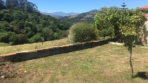 A rural landscape with a stone wall, trees, and distant mountains. - Casa Rural Luey (luey)