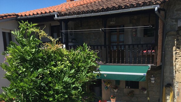A rustic building with a tiled roof, a green awning, and a stone wall. - Casa Rural Luey (luey)