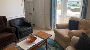 Ett vardagsrum med en brun soffa, en svart läderfåtölj och en beige soffa med en blå kudde. Där finns också ett träbord med en dekorativ prydnad på.