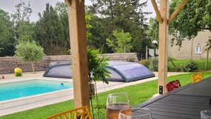 Un espace extérieur aménagé, abrité et doté de sièges, avec une piscine en arrière-plan.