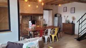 Un espace de vie chaleureux avec une table à manger en bois, des chaises colorées, un canapé agrémenté de coussins décoratifs et un coin cuisine équipé d’un réfrigérateur et d’un four à micro-ondes.