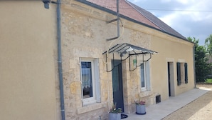 Un bâtiment doté d’une façade en pierre, d’un porche carrelé et d’une véranda couverte ornée de plantes en pot.