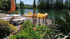 A lakeside patio with yellow lounge chairs, a table, and an umbrella.