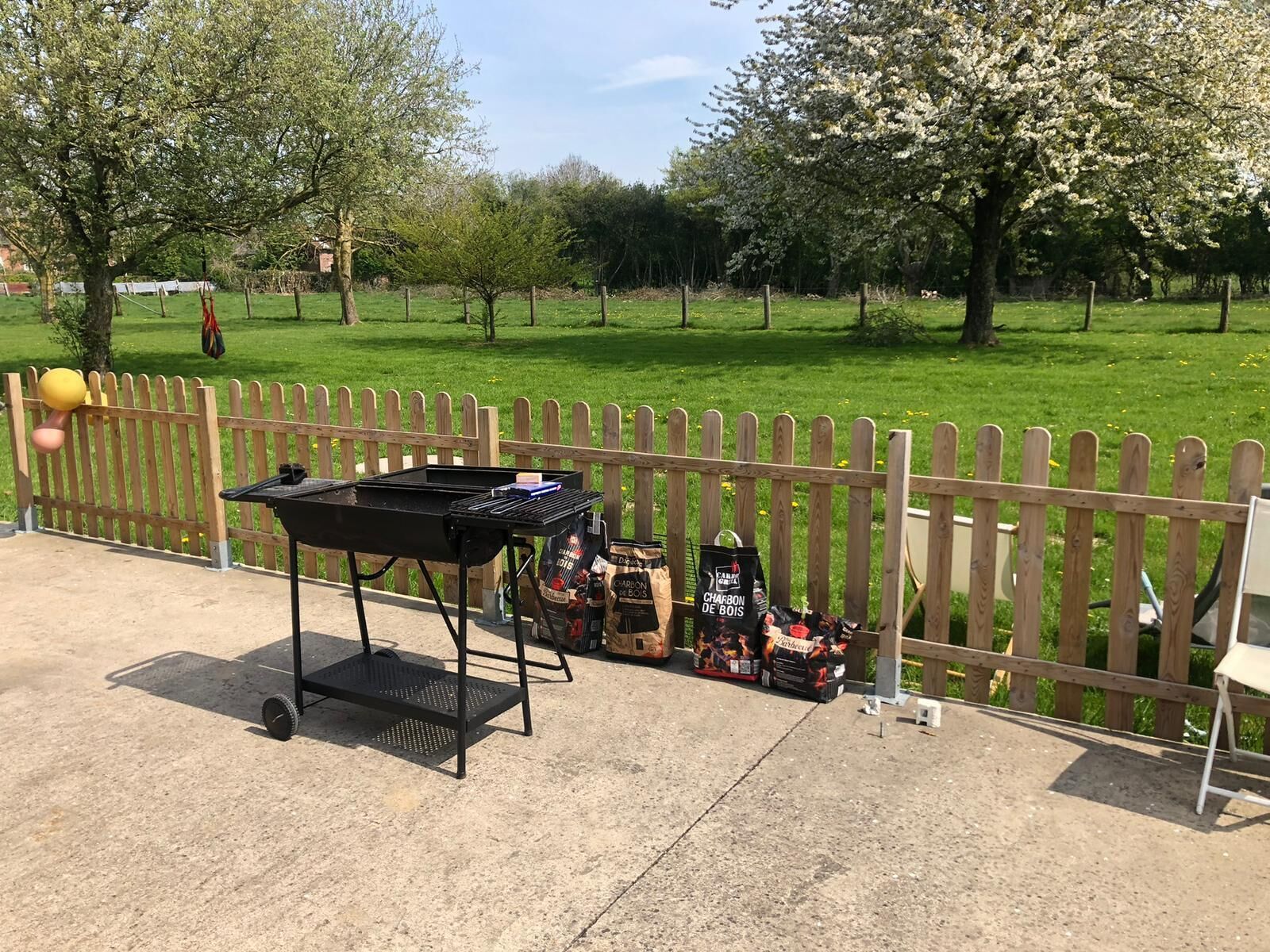 A barbecue grill with charcoal bags and a wooden fence in a park.