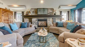A cozy living room with two sofas, a fireplace, and a stone wall. - Lakefront View w Private BEACH! - Spacious Luxury Estate Home ~ Pet Friendly (Port Stanley)