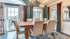 A dining area with a wooden table, upholstered chairs, and hanging spherical light fixtures. - Lakefront View w Private BEACH! - Spacious Luxury Estate Home ~ Pet Friendly (Port Stanley)