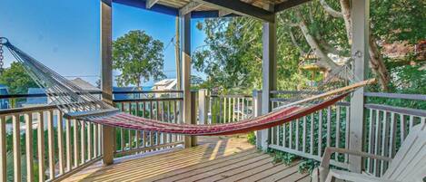 A hammock on a wooden deck with a view of trees and a clear sky.