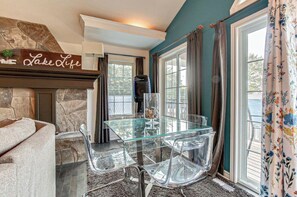 A dining area with a glass table and chairs, a stone fireplace, and a view of the outdoors.