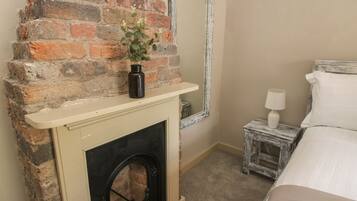 A bedroom with a brick fireplace, a small bedside table with a lamp, and a bed with white bedding.