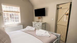 A bedroom with a bed, a dresser, a TV, and a door. - Number 6 (Telford)