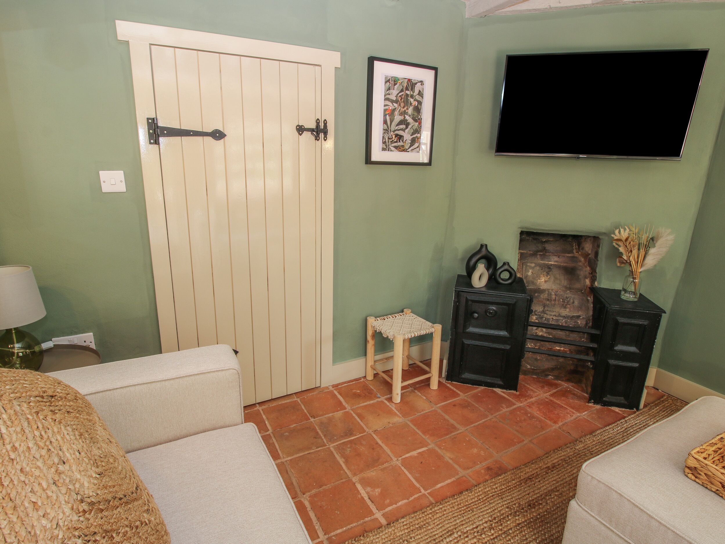 A living room with a white door, a small stool, a fireplace, a television, and a woven rug.