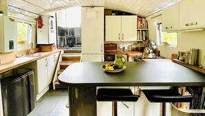 A compact kitchen with a central island, white cabinets, and a small dining area with two stools. - Boutique Boat Stays Contemporary Barge (Bath)