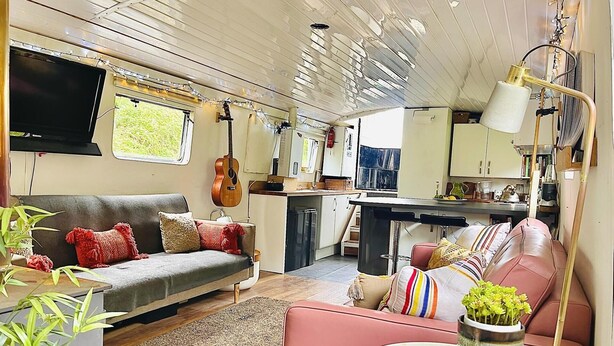 A compact RV interior with a sofa, a dining table, a kitchen area, and a mounted TV. - Boutique Boat Stays Contemporary Barge (Bath)
