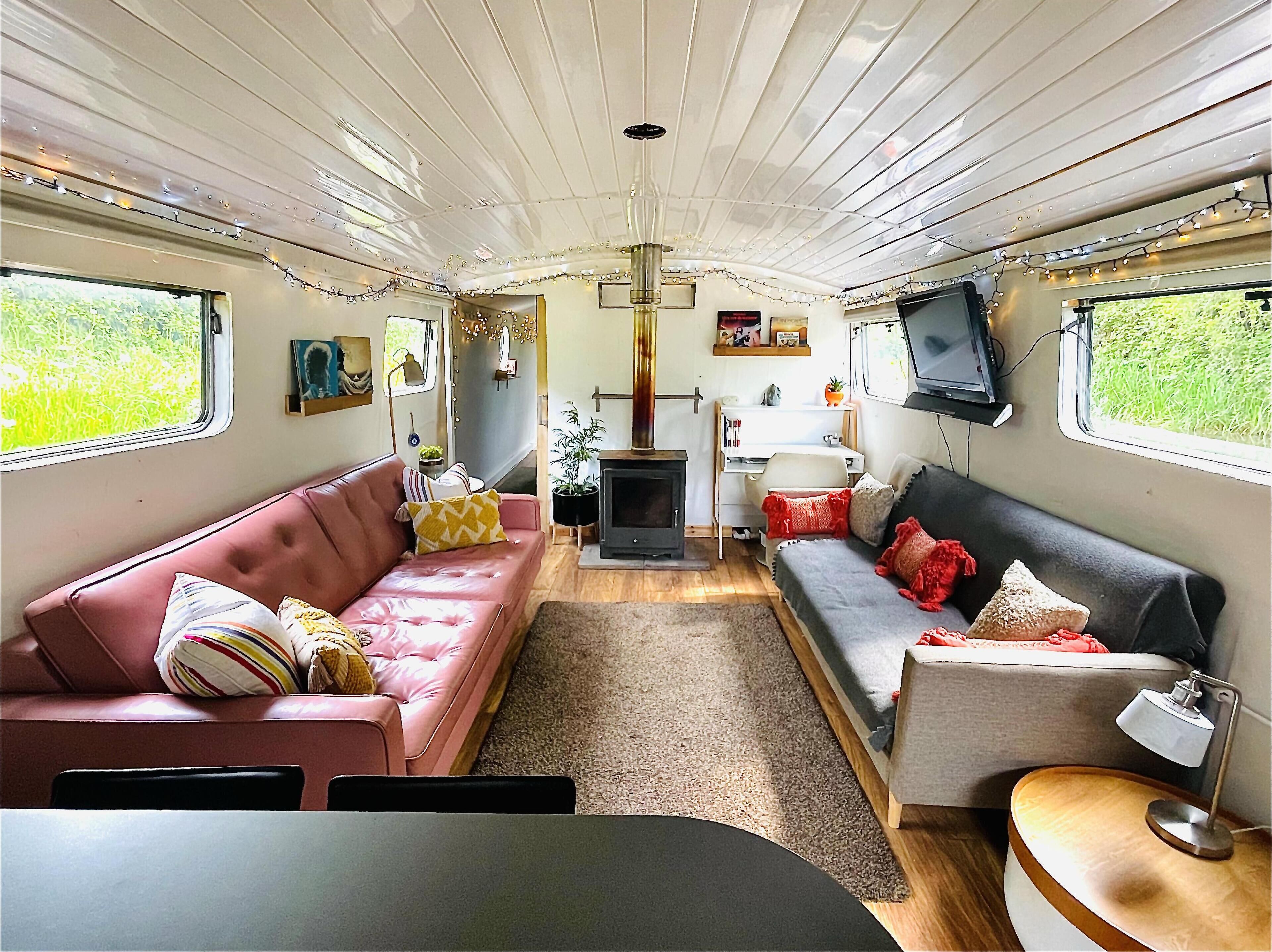 Un interior de autocaravana acogedor con un sofá rosa y gris, una mesita, un televisor y un estufa de leña.