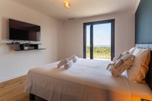 A hotel room with a bed, a flat-screen TV, a balcony with a view, and a ceiling light.