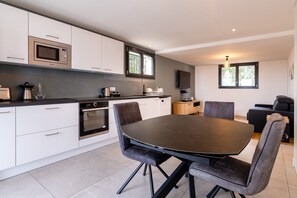 A modern kitchen with white cabinetry, a built-in oven, and a dining area with a dark table and grey upholstered chairs.