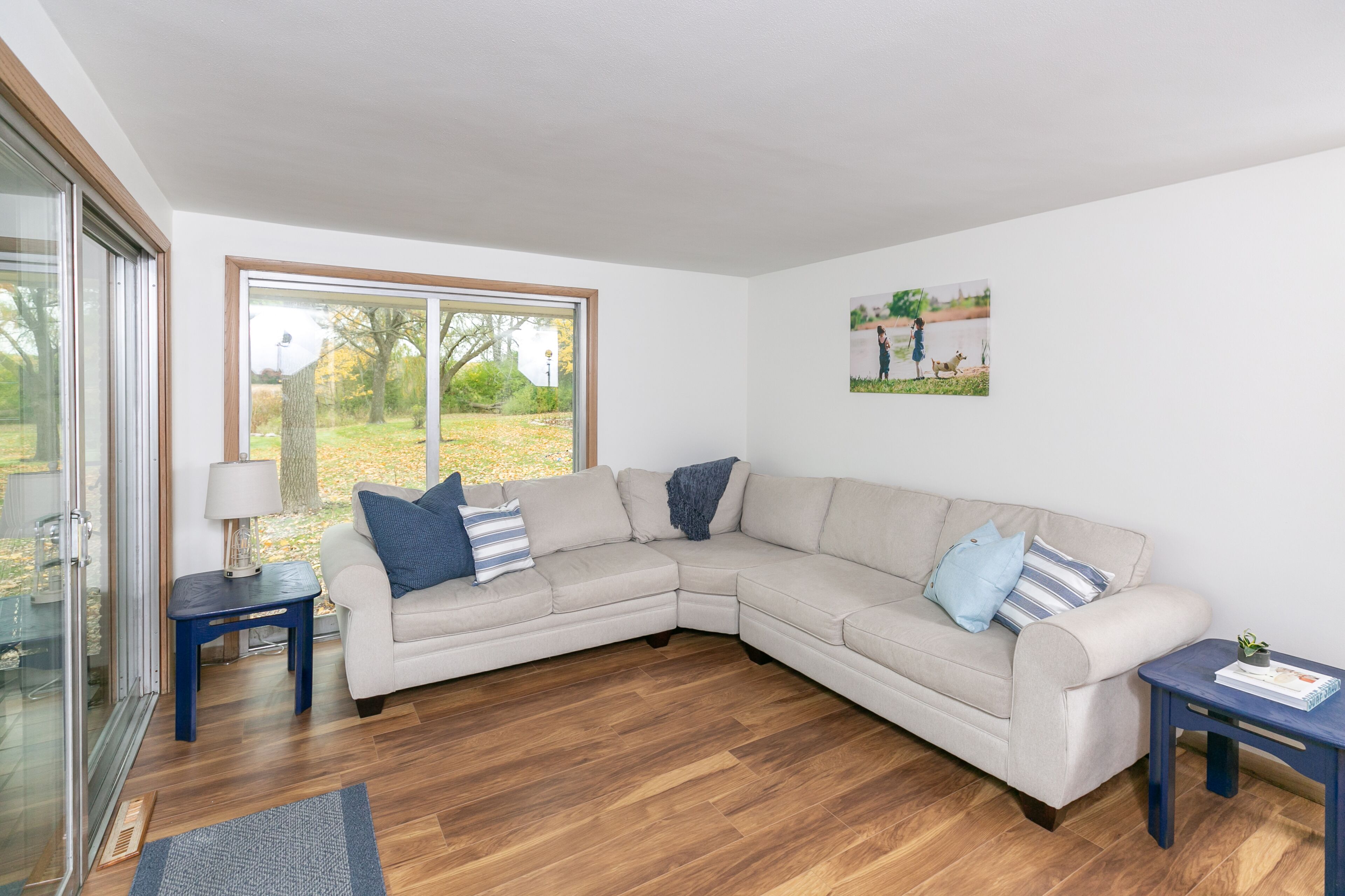 A modern living room with a beige sectional sofa, two side tables, and a glass door leading to a garden.