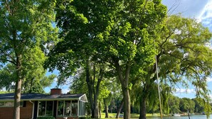A house with a covered porch, surrounded by lush green trees and a lake.